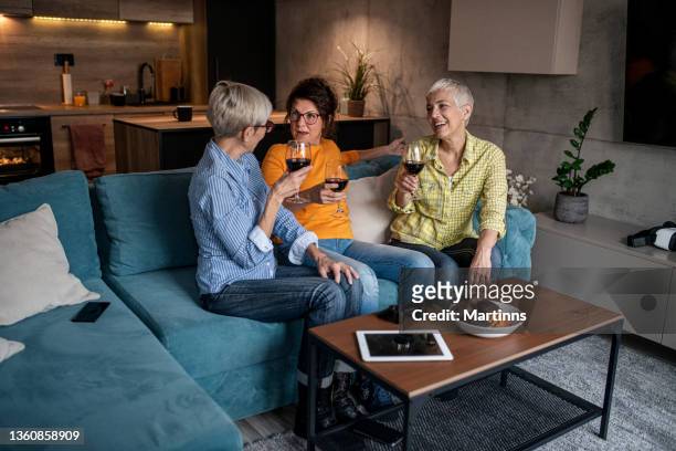 three senior women drinking wine in the living room after playing video games - three people on couch stock pictures, royalty-free photos & images
