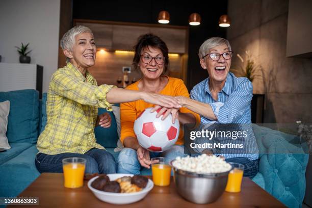 drei ältere frauen, die fußballspielen im fernsehen schauen und spaß im wohnzimmer haben - fußball fan oma stock-fotos und bilder