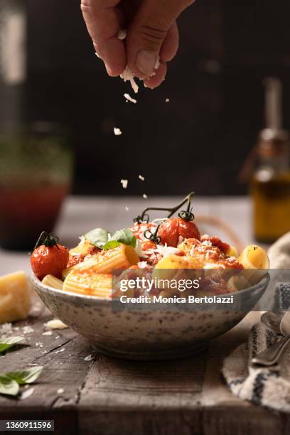 tomato sauce bowl of rigatoni, with human hand, olive oil, and parmisan cheese - photograph on table stock-fotos und bilder