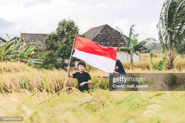 a kid with his muslim  sister holding indonesia flag in the village - indonesia flag stock pictures, royalty-free photos & images