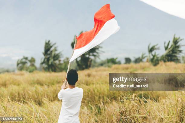 asian young adult holding indonesia flag in the village - indonesia flag stock pictures, royalty-free photos & images