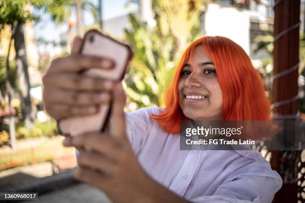 young woman taking a selfie or filming outdoors - oranje haar stockfoto's en -beelden