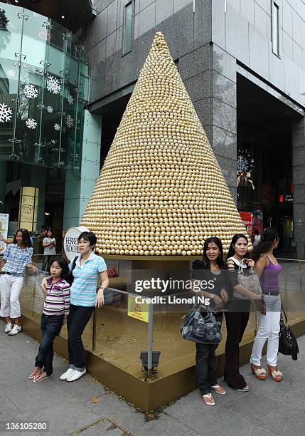 People pose with a christmas tree made up of Ferrero Rocher chocolates at a Orchard Road shopping mall at The Heeren on December 25, 2011 in...