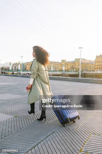 young curly-haired latin girl, businesswoman and entrepreneur traveling from one city to another for her work. traveler woman walking with a suitcase in the city - busy lobby stock pictures, royalty-free photos & images