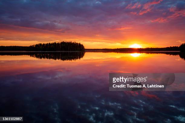 scenic and beautiful sunset and colorful, dramatic cloudy sky and their reflections on a calm lake in finland at summer. - midsummer finland stock pictures, royalty-free photos & images