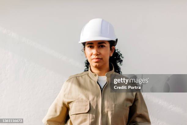 porträt einer hispanischen elektrikerin in uniform und schutzhelm - bauhelm stock-fotos und bilder