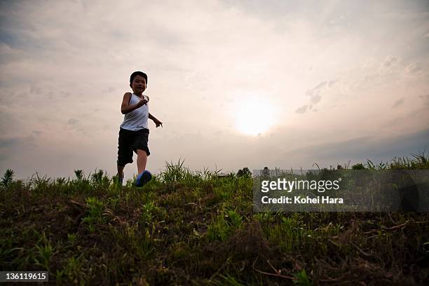 boy running on grass field at dusk - forward athlete stock-fotos und bilder