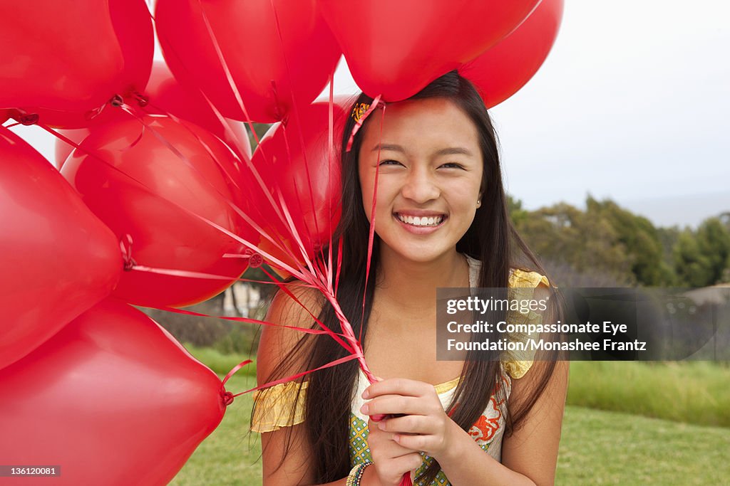 Teenage girl in garden, holding bunch of balloons