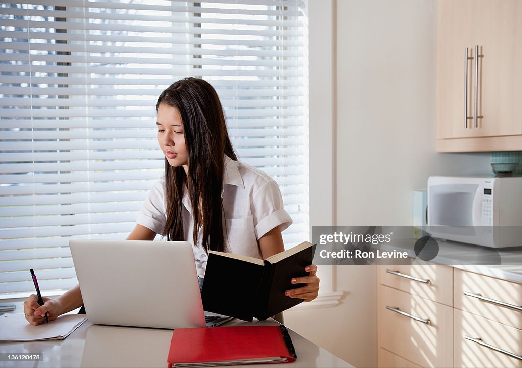 Teen girl doing homework in kitchen