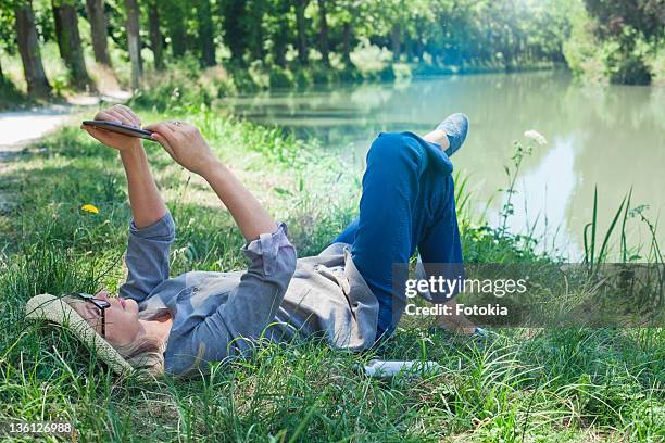 woman reading e book in shady spot. - spot lit photos et images de collection