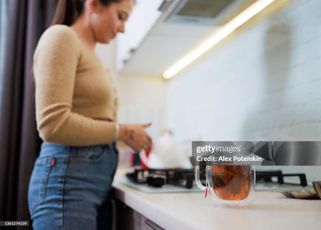Une jeune femme prépare du thé dans la cuisine moderne. Elle utilise un sachet de thé et le fait directement dans une tasse. Focus sélectif sur une tasse de thé au premier plan.