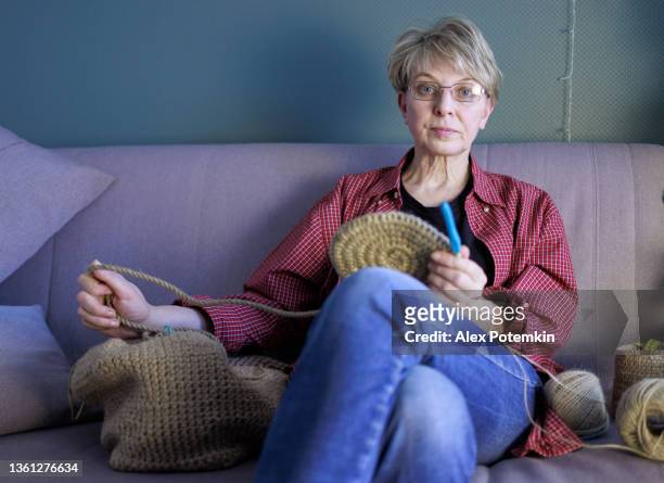 atractiva mujer madura de 54 años haciendo ganchillo, haciendo una canasta de yute hecha a mano. - 50 54 years fotografías e imágenes de stock