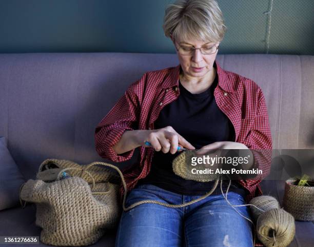 attractive mature 54-years-old woman doing crocheting, making a hand-made jute basket. - 50 54 years stockfoto's en -beelden