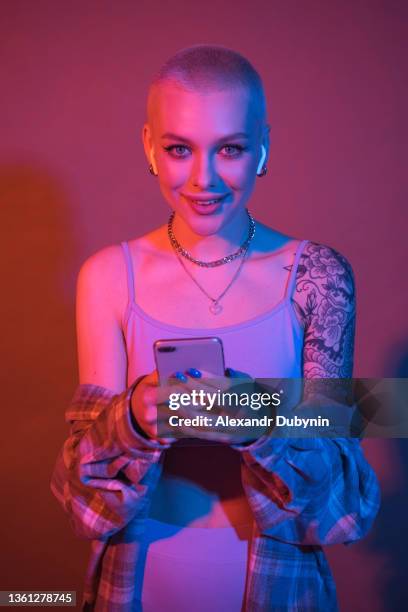 stylish young woman listening to music through headphones using phone in color neon light smiling - concert face stock pictures, royalty-free photos & images