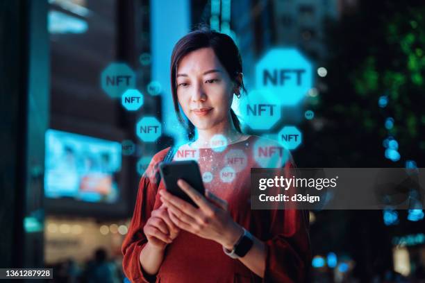 young asian woman using smartphone in downtown city street at night, working with blockchain technologies, investing or trading nft (non-fungible token) on cryptocurrency, digital asset, art work and digital ledger - bid data stock pictures, royalty-free photos & images