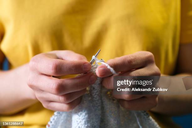 the girl is holding a knitting project and metal knitting needles in close-up. a woman knits a blue wool sweater or scarf, sitting on the couch at home. the concept of hobbies, creativity, needlework and manual work. creating clothes with your own hands. - knitting needles stock-fotos und bilder