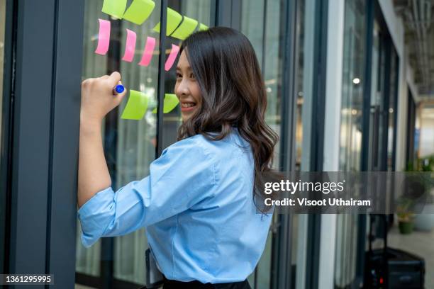 young female in the office glues sticky sheets on the glass partition of the office of a large company. - scrummen stockfoto's en -beelden