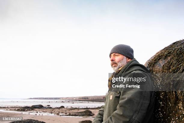 portrait of a mature man on a beach in the winter. - ijsmuts stockfoto's en -beelden