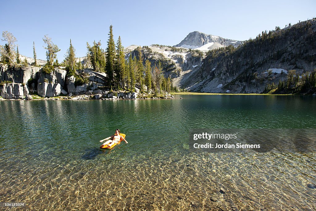 A female uses her sleeping pad to float in a lake.