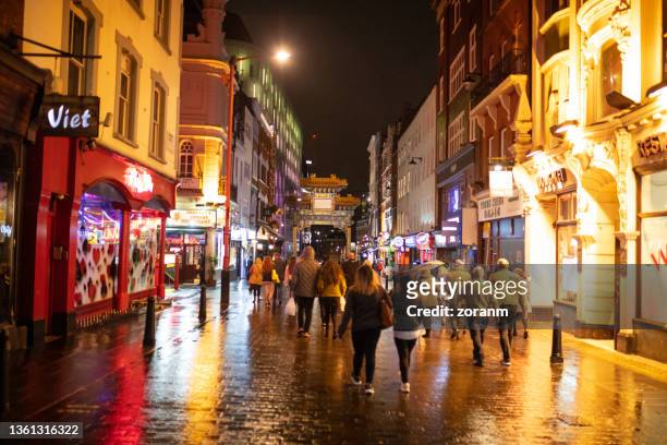 people walking on wet gerrard street towards chinatown gate - soho london night stock pictures, royalty-free photos & images