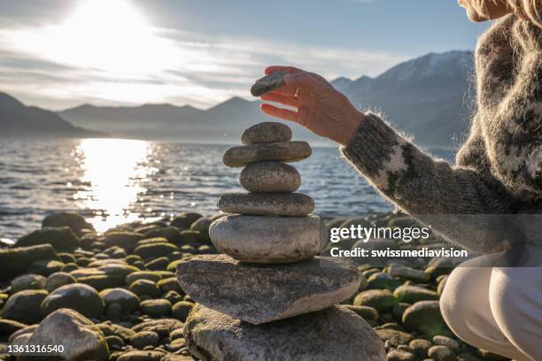 feche acima na mão da mulher empilhando pedra perto do lago - stack rock - fotografias e filmes do acervo