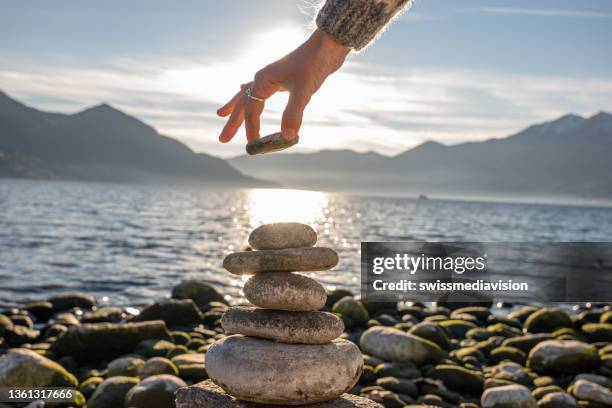 close up on woman's hand stacking rock by the lake - rock terrain stockfoto's en -beelden