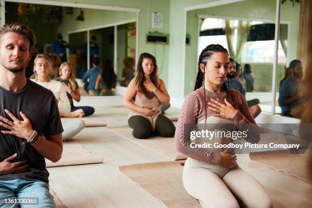 yoga students meditating and touching their chakras during a class - meditating stockfoto's en -beelden