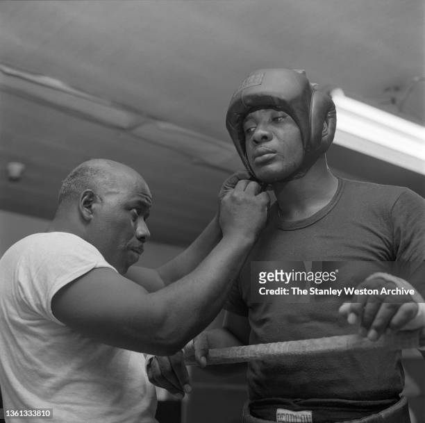 Trainer Dick Sadler tightens Charles L. "Sonny" Liston's head gear while training on October 01, 1954 in Philadelphia, Pennsylvania.