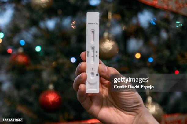 detail of a hand holding a positive covid antigen test with a christmas tree in the background. - christmas kit photos et images de collection