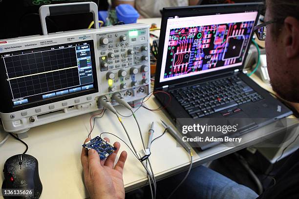 Particpant checks a circuit board next to an oscilloscope on the first day of the 28th Chaos Communication Congress - Behind Enemy Lines computer...