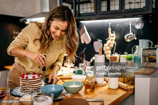 smiling woman applying icing on pancake cake - pastry chef stock pictures, royalty-free photos & images