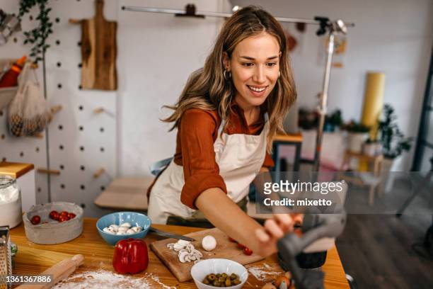 bloguera de comida preparando pizza y grabando video en un teléfono inteligente - mujer cocinando fotografías e imágenes de stock