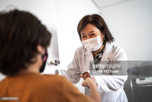 doctor greeting a boy with a fist bump at a medical clinic - using a facial mask - smile mask stock pictures, royalty-free photos & images