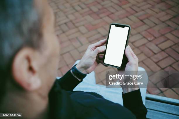 man sits on bench outdoors holding smart phone with blank screen - holding iphone screen stock pictures, royalty-free photos & images