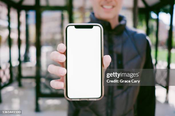 man stands at bus stop holding smart phone with blank screen - man showing phone photos et images de collection