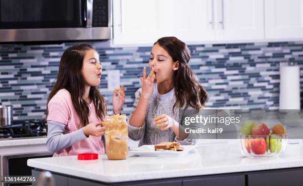 multirassische zwillingsschwestern essen erdnussbutter-sandwiches - erdnussbutter stock-fotos und bilder