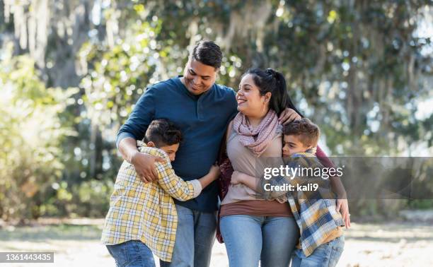 hispanische familie mit zwei jungen geht im park spazieren und umarmt sich - lateinamerikanische abstammung stock-fotos und bilder