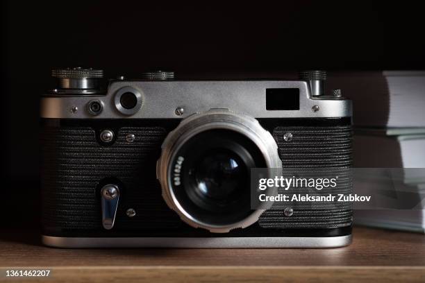 an old retro film camera. a vintage camera and a stack of books on a wooden shelf. the photographer's subjects at the workplace. the concept of hobbies, professional photo services. acquisition of the skill of photographing, learning from books. - maquina fotografica antiga imagens e fotografias de stock