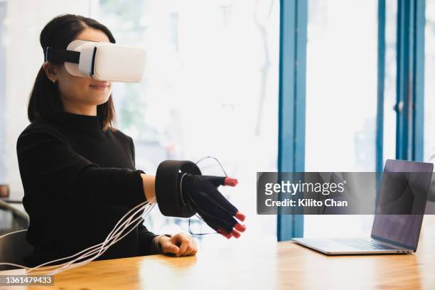 asian woman wearing vr headset and haptic glove interacting with virtual object/person in the metaverse - realtà aumentata foto e immagini stock