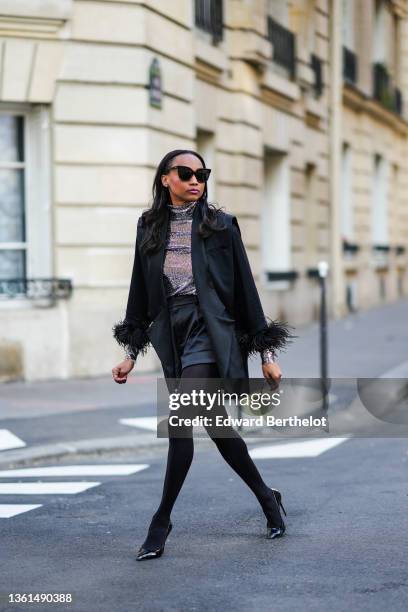 Emilie Joseph wears black sunglasses, a silver turtleneck sequined long sleeves top from Maje, a black sleeveless oversized silk / satin blazer...