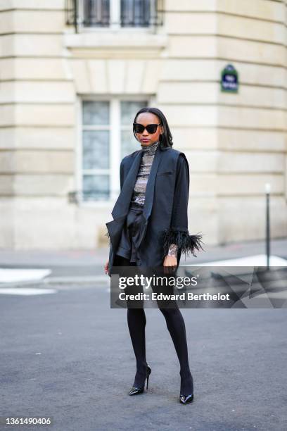 Emilie Joseph wears black sunglasses, a silver turtleneck sequined long sleeves top from Maje, a black sleeveless oversized silk / satin blazer...