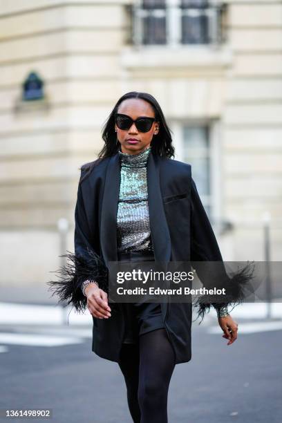 Emilie Joseph wears black sunglasses, a silver turtleneck sequined long sleeves top from Maje, a black sleeveless oversized silk / satin blazer...