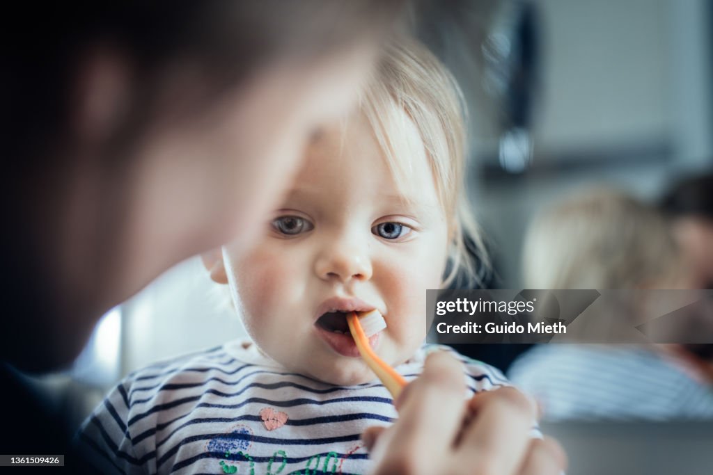 Mother brushing teeth of her toddler girl in the evening.