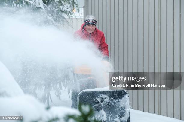 senior gray-haired woman with a red jacket uses a yellow snow blower on a cold and snowy day in norway gray-haired woman with a red jacket uses a yellow snow blower on a cold and snowy day in norway - finn bjurvoll stock pictures, royalty-free photos & images