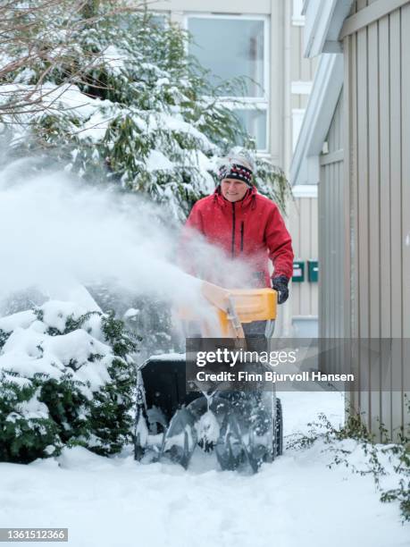 senior gray-haired woman with a red jacket uses a yellow snow blower on a cold and snowy day in norway gray-haired woman with a red jacket uses a yellow snow blower on a cold and snowy day in norway - finn bjurvoll stock pictures, royalty-free photos & images