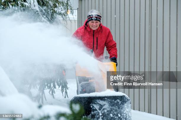 senior gray-haired woman with a red jacket uses a yellow snow blower on a cold and snowy day in norway gray-haired woman with a red jacket uses a yellow snow blower on a cold and snowy day in norway - finn bjurvoll imagens e fotografias de stock