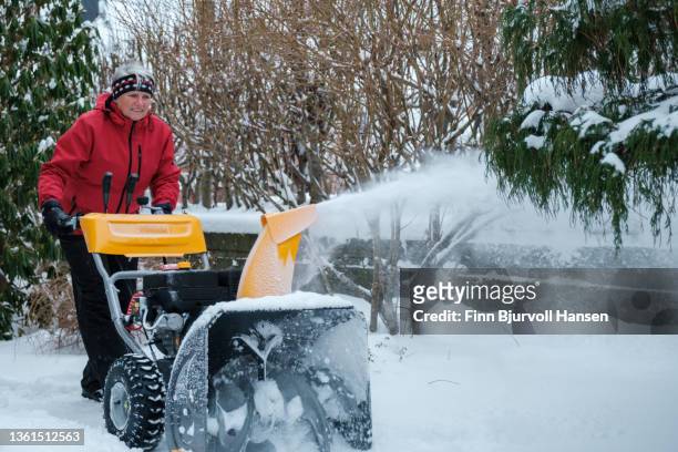 senior gray-haired woman with a red jacket uses a yellow snow blower on a cold and snowy day in norway gray-haired woman with a red jacket uses a yellow snow blower on a cold and snowy day in norway - finn bjurvoll stock pictures, royalty-free photos & images