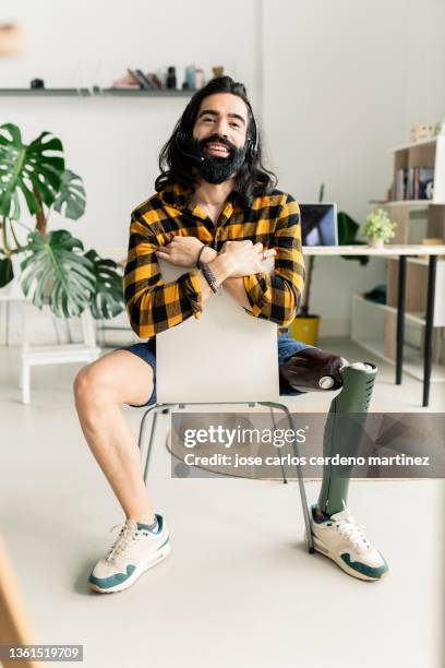 man with a leg prosthesis sitting on a chair at home happy smiling - fake man stockfoto's en -beelden