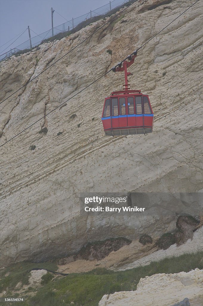 Red cable car in front of white cliffs.
