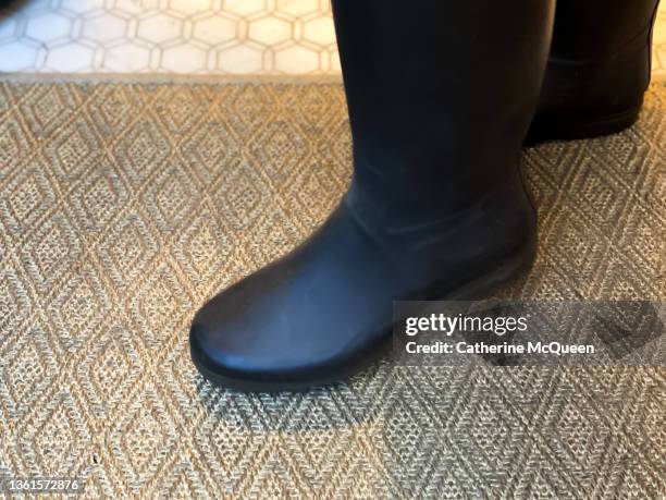 female wipes rain boots on front door doormat - mud floor stock pictures, royalty-free photos & images